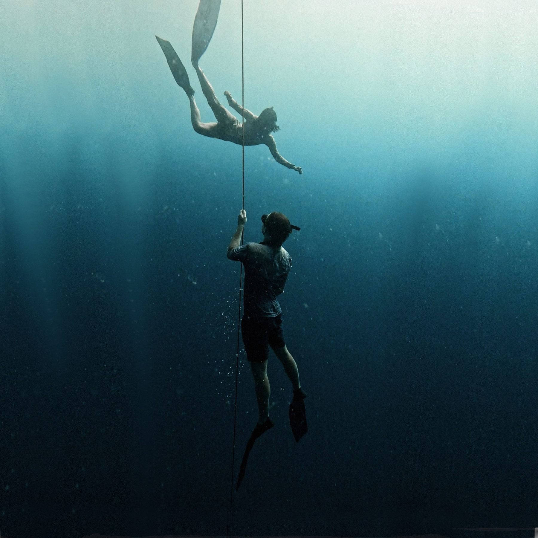 A freediver descending along a line into deep, calm water